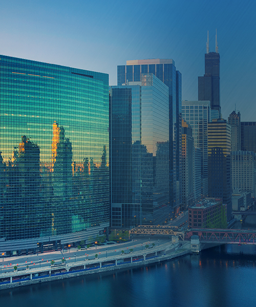 Modern city skyline reflecting the sunset on a riverfront, showcasing a mix of architectural styles.