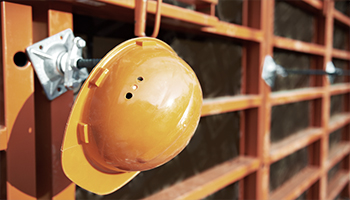 A yellow hard hat hanging on a hook against a storage background.