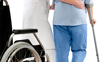 A patient with a crutch being assisted by a nurse beside a wheelchair.