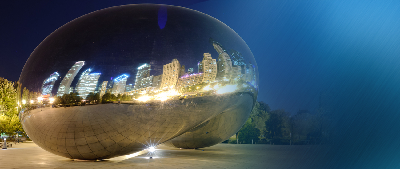 A reflective spherical sculpture capturing the city skyline at night, with lights creating a starburst effect on the ground.